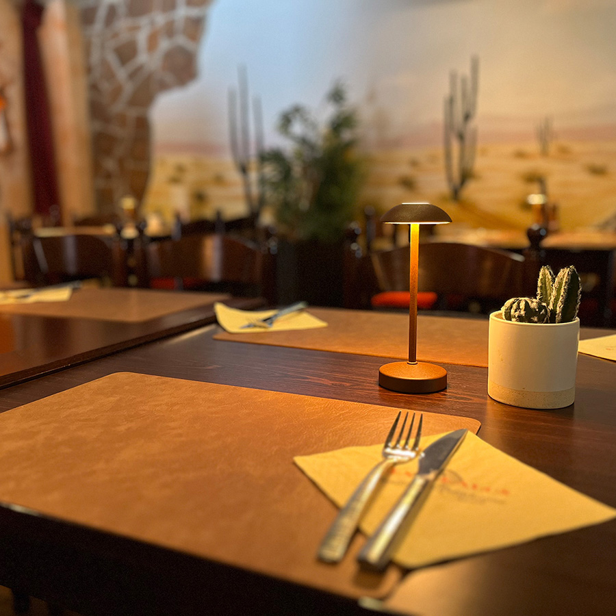 bilder-teaser Gemütliches Restaurant mit stilvollem Tisch, Besteck und dekorativem Kaktus im Hintergrund.
